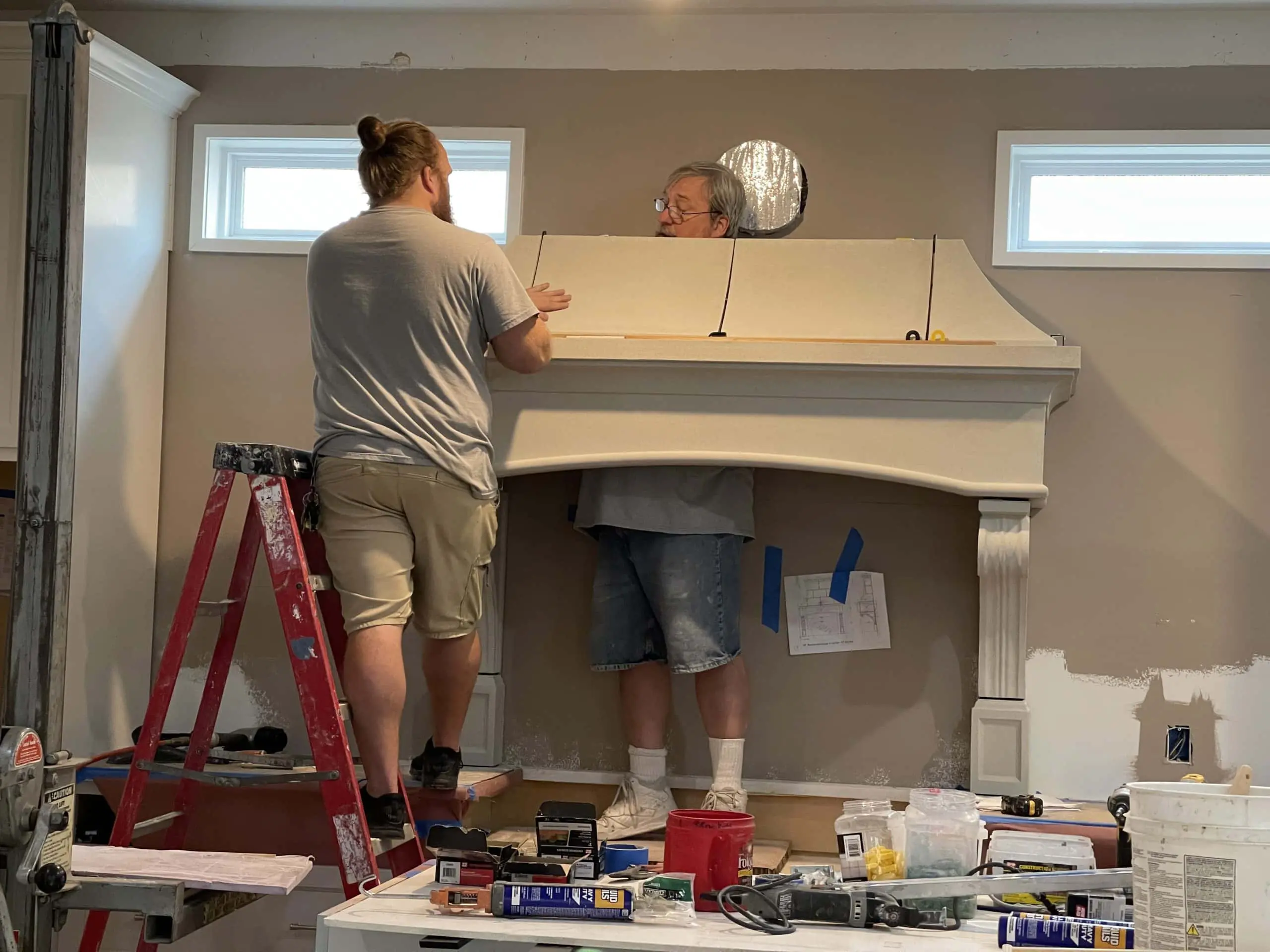 Two workers in the process of installing a cast stone kitchen range hood.